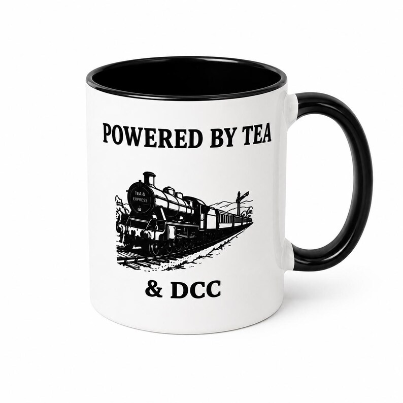 K&ouml;nnte beinhalten: Ein wei&szlig;er Keramikbecher mit schwarzem Innenraum und Henkel. Die Vorderseite zeigt eine schwarze Grafik einer Dampflokomotive mit dem Text "POWERED BY TEA" &uuml;ber dem Zug und "& DCC" darunter. Der Zug tr&auml;gt die Aufschrift "TEA & EXPRESS" vorne.