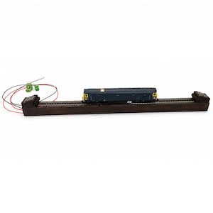 May include: A model diesel locomotive in dark blue and yellow sits on a straight section of model train track mounted on a dark wooden base. The track features buffer stops at both ends and includes red and black electrical wiring with green connectors.