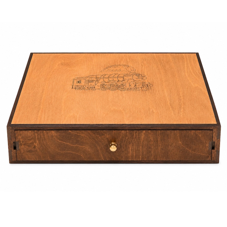 Op de afbeelding: Een houten kist met een lade, met een gedetailleerde gegraveerde afbeelding van een stoomtrein op het deksel. De kist heeft een lichtbruine bovenkant en een donkerdere bruine lade met een goudkleurige knop. De tekst "LNER" is zichtbaar.
