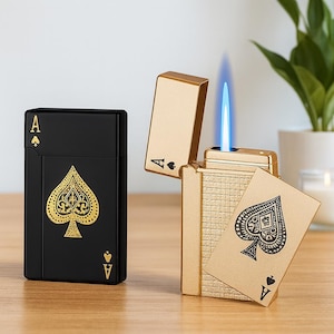 May include: A black and gold Ace of Spades lighter with a gold Ace of Spades card. The lighter is rectangular with a gold spade design. A gold lighter is open with a blue flame. The Ace of Spades card is also gold.