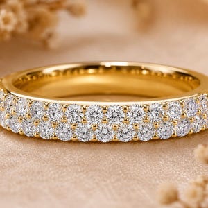 Könnte beinhalten: Ein Ring aus Gelbgold mit zwei parallelen Reihen kleiner, runder, klarer und facettierter Steine, die auf der Außenfläche eingefasst sind. Das Metall hat eine polierte, reflektierende Oberfläche und die Steine sind in einem durchgehenden, gleichmäßigen Muster angeordnet.