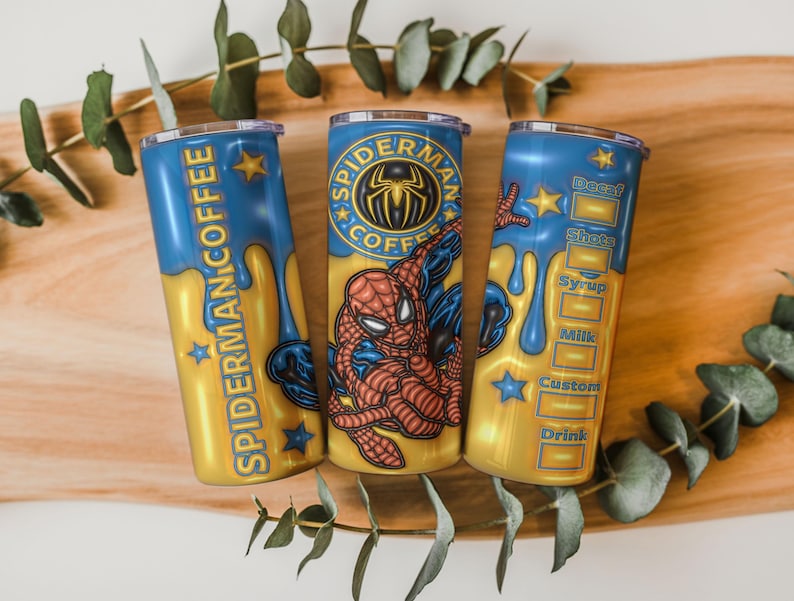 May include: Three custom coffee tumblers with a Spider-Man theme. The tumblers are blue and gold, with the words "Spider-Man Coffee" and a Spider-Man logo. One tumbler has a drink customization menu.