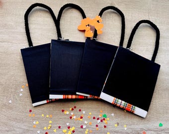May include: Four rectangular black fabric pouches with black fuzzy handles. Each pouch features a horizontal strip of orange, green, and white plaid fabric at the bottom edge. A cluster of small orange heart-shaped cutouts is attached to one handle.