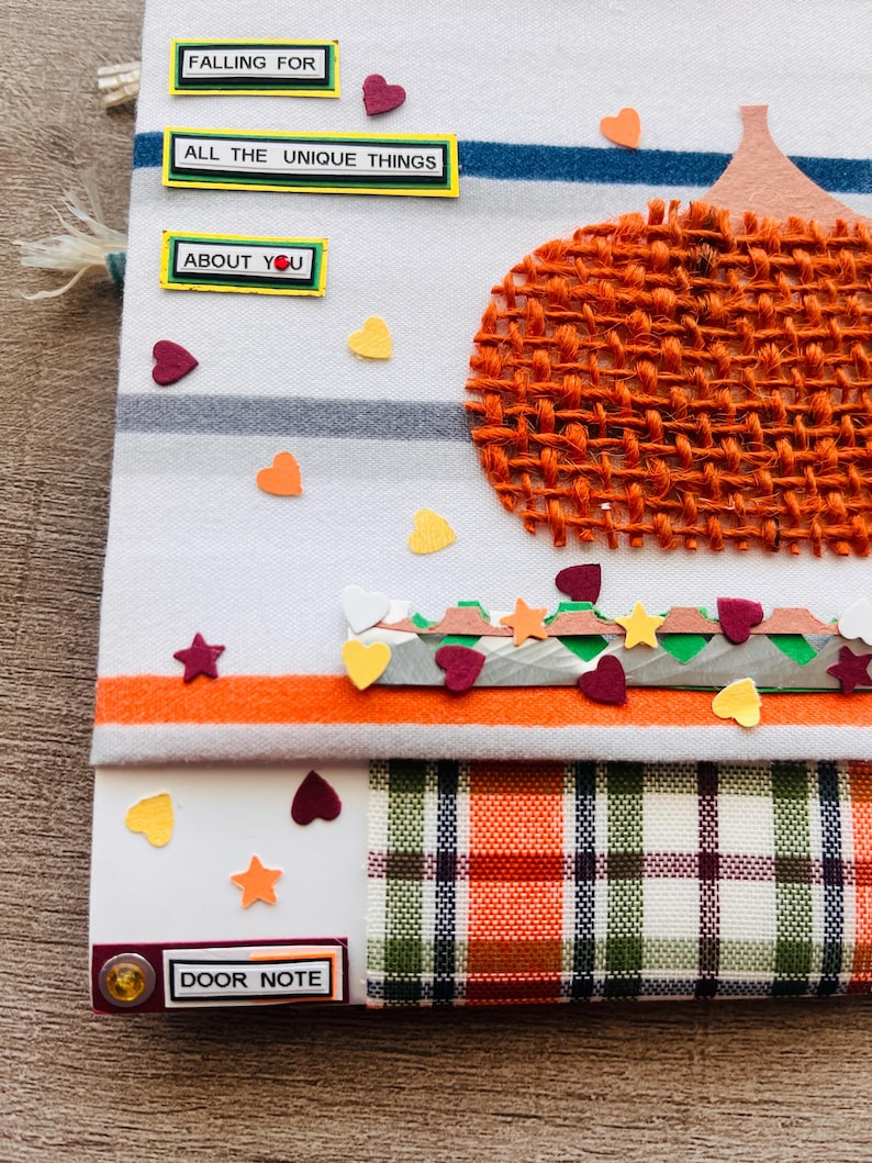 May include: A fabric door note featuring a burlap pumpkin, horizontal stripes, and scattered heart and star cutouts. Text labels read FALLING FOR, ALL THE UNIQUE THINGS, ABOUT YOU, and DOOR NOTE. The base includes a plaid pattern in orange and green.