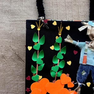 May include: A black fabric tote bag featuring a decorative applique design. The scene includes two green vine stalks with heart-shaped leaves, orange heart-shaped pumpkins, and a small scarecrow figure wearing a blue shirt and denim pants.