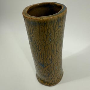 May include: A handmade, cylindrical ceramic vase with a textured, tree-like pattern. The vase is primarily brown with blue accents and a slightly irregular rim. The vase is suitable for displaying flowers or as a decorative item.