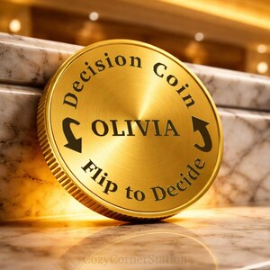 May include: A circular gold-colored metal decision coin featuring the text Decision Coin at the top and Flip to Decide at the bottom. The center of the coin is engraved with the name OLIVIA in capital letters, flanked by two curved arrows.