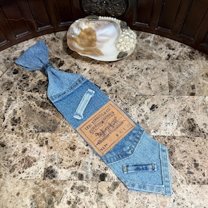 May include: A denim tie with a Levi Strauss & Co. label. The tie is made from blue denim fabric and features a classic tie shape. The label includes the text "517" and measurements "W 42 L 32".