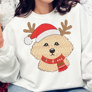 May include: A white crewneck sweatshirt featuring an embroidered graphic of a tan curly-haired dog wearing a red and white Santa hat with brown reindeer antlers and a red, green, and white patterned winter scarf around its neck.