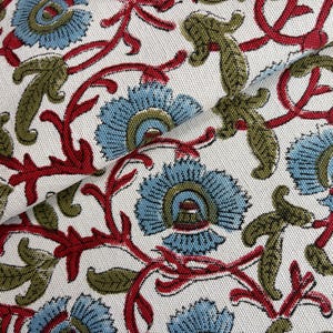 May include: A white fabric featuring a repeating floral pattern with light blue petals, olive green leaves, and dark red stems. The textile has a visible woven texture and a dense arrangement of botanical motifs across the entire surface area.