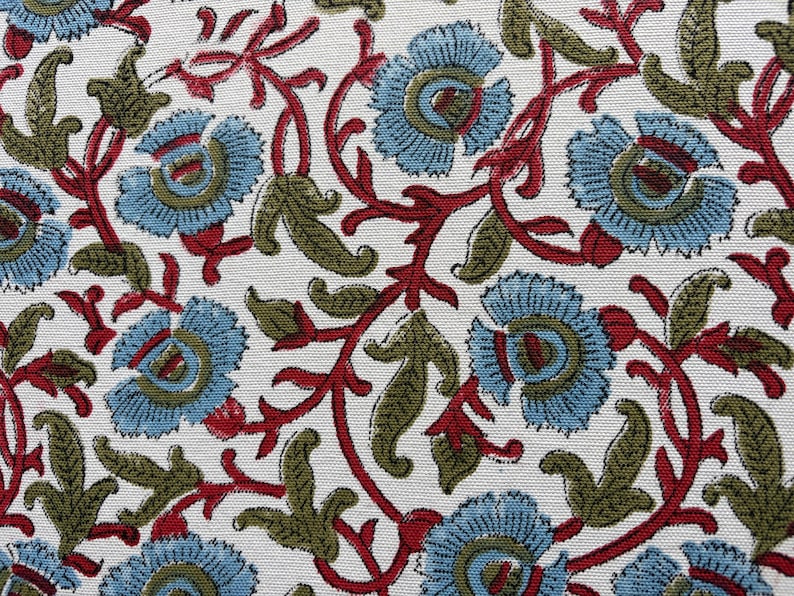 May include: A white fabric featuring a repeating floral pattern with light blue blossoms, olive green leaves, and thin red winding stems. The design is printed across the surface, showcasing a dense arrangement of botanical elements and vines.