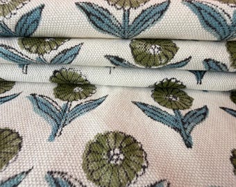 May include: Close-up of folded fabric with a repeating floral pattern. The flowers are olive green with white centers, and the leaves and stems are teal. The background is a cream color, and the fabric appears to be a woven cotton or linen.