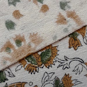 Puede incluir: Primer plano de dos piezas de tela con estampados florales. Una tiene un patrón repetido de formas florales marrones y verdes sobre un fondo crema. La otra tiene un diseño floral más grande con contornos negros y detalles amarillos y verdes.