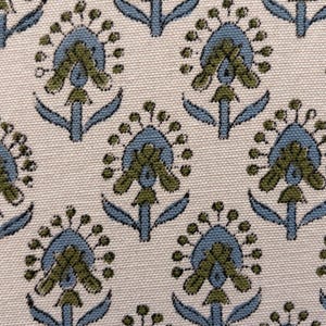 May include: Close-up of a fabric with a repeating floral pattern. The design features stylized flowers in shades of blue and olive green against a cream-colored background. The fabric has a textured appearance.