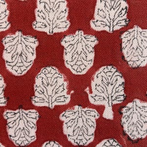 Peut inclure: Gros plan sur un tissu avec un motif répété de formes blanches en forme de feuilles sur un fond rouge foncé. Les feuilles ont des détails noirs complexes, créant un design texturé. Le tissu semble être du coton ou une matière similaire.
