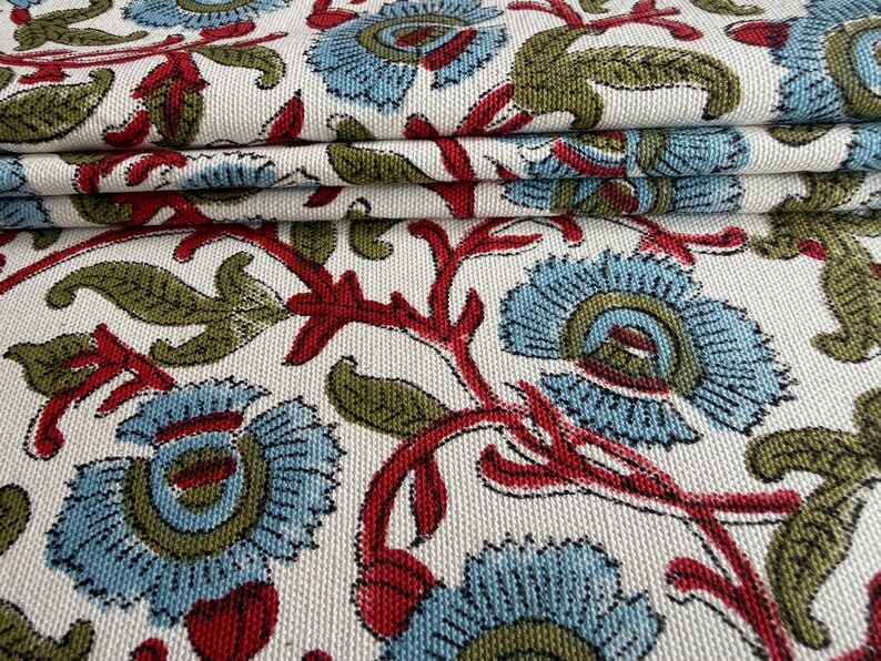 May include: A woven fabric featuring a repeating floral pattern on an off-white background. The design consists of light blue flowers with olive green centers, connected by deep red stems and olive green leaves, creating a dense botanical motif.