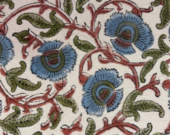 May include: Close-up of a fabric with a floral pattern. The design features blue flowers with green and red accents on a cream-colored background. The flowers are surrounded by green leaves and red stems.