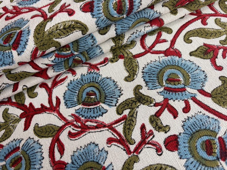 May include: A woven fabric featuring a repeating floral pattern on an off-white background. The design consists of light blue stylized flowers with olive green leaves and thin red stems, creating a dense, textured botanical print across the surface.