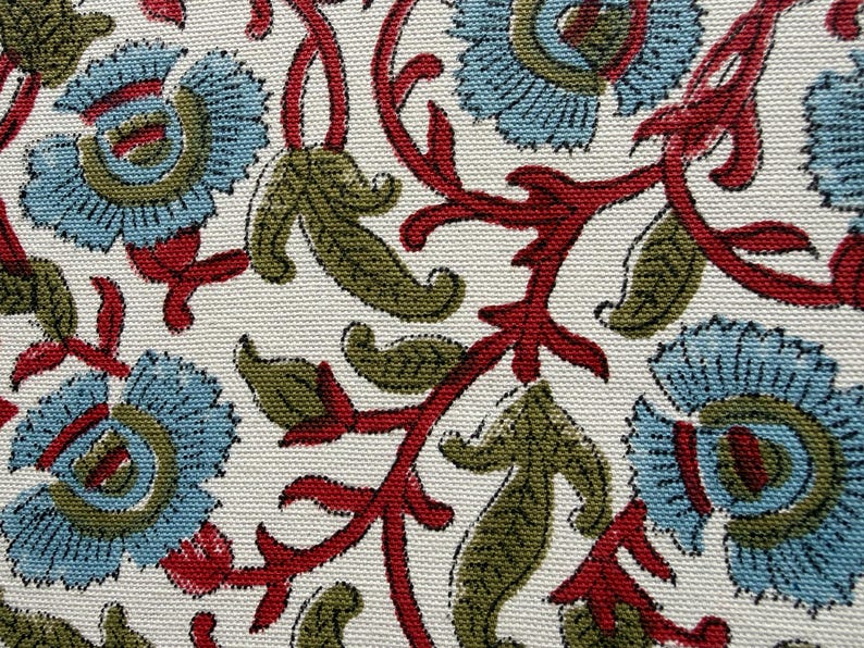May include: A textile fabric featuring a repeating floral pattern with light blue petals, olive green leaves, and dark red stems on a white background. The material has a visible woven texture, showcasing a detailed botanical print design.