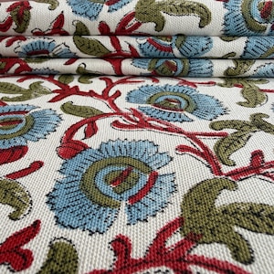May include: A woven fabric featuring a repeating floral pattern on an off-white background. The design consists of light blue flowers with olive green centers, connected by vibrant red stems and olive green leaves, creating a textured surface.