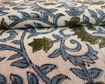 May include: Close-up of a folded fabric with a repeating floral pattern. The design features blue and olive green leaves and vines on a cream-colored background. The fabric has a textured appearance.