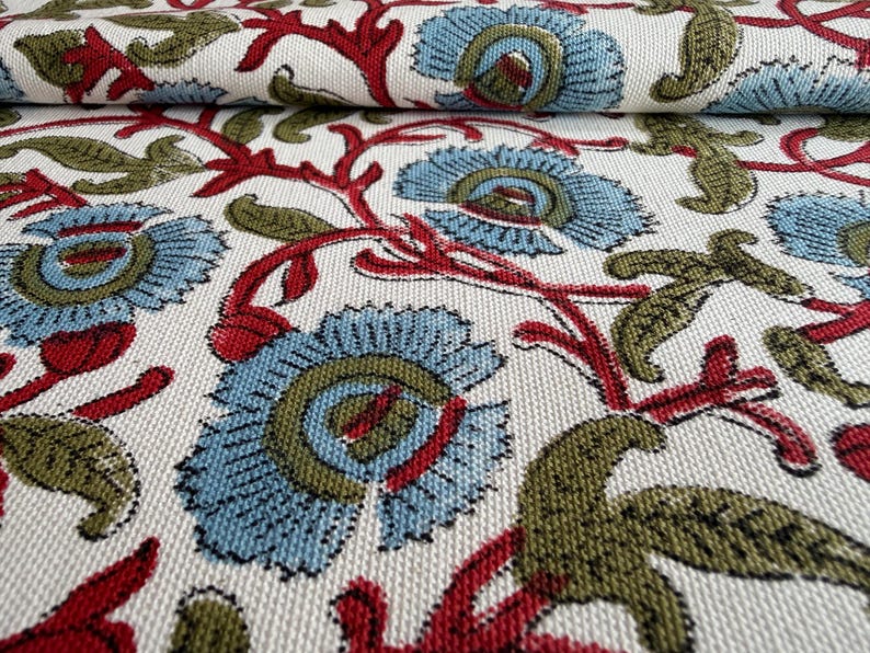 May include: A woven fabric featuring a repeating floral pattern on an off-white background. The design consists of light blue flowers with olive green centers, connected by vibrant red stems and accented with olive green leaves throughout.