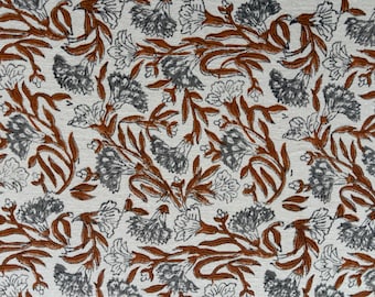 May include: Close-up of a fabric with a repeating floral pattern. The design features gray and white flowers with rust-colored stems and leaves against a cream-colored background. The pattern is dense and detailed.