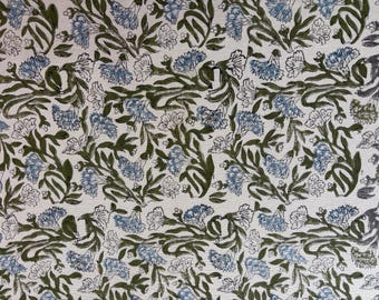 May include: Floral fabric with a repeating pattern of blue and white flowers and green leaves on a cream background. The design is a stylized botanical print, suitable for textiles or wallpaper.