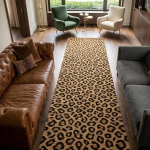 May include: A long rectangular area rug featuring a repeating leopard print pattern in shades of tan, brown, and black. The rug is positioned on a dark wood floor between a brown leather tufted sofa and a gray upholstered sofa in a living room.