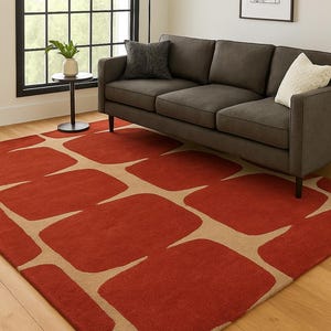 Può includere: Un moderno tappeto con un audace motivo geometrico. Il tappeto presenta grandi forme irregolari in un rosso vibrante, contrastate da uno sfondo beige neutro. Il tappeto è in un soggiorno con un divano grigio scuro.
