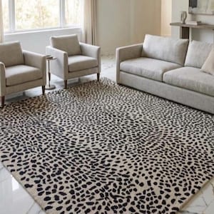 May include: A large rectangular area rug featuring a dense, repeating black spotted pattern on a light beige background. The rug is positioned on a white marble floor in front of two light-coloured armchairs and a matching three-seat sofa.