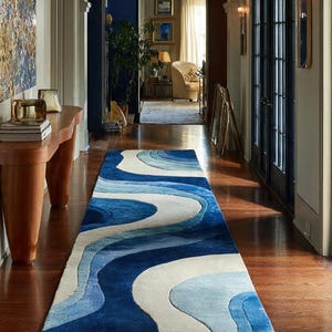 May include: A long, rectangular rug with a wavy design in shades of blue and white. The rug is placed on a hardwood floor in a hallway, adding a decorative element to the space. The rug's design resembles ocean waves.