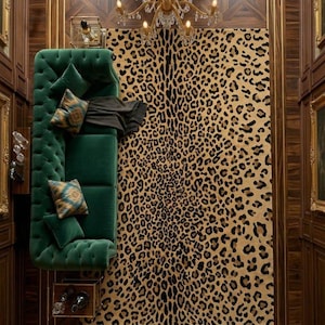 May include: A rectangular area rug featuring a tan and black leopard print pattern. The rug is positioned next to a deep green tufted velvet sofa adorned with patterned throw pillows and a dark grey throw blanket, set beneath a gold chandelier.