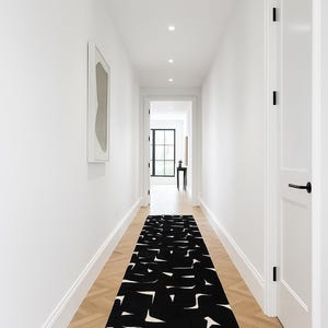 Könnte beinhalten: Ein langer, schwarz-weiß gemusterter Läufer in einem Flur mit weißen Wänden und hellem Holzboden. Der Teppich hat ein abstraktes Design. Der Flur hat Einbaustrahler und ein gerahmtes Kunstwerk an der Wand.