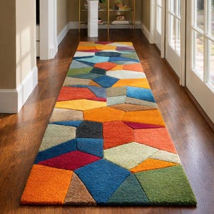 May include: A colourful, rectangular rug featuring a geometric design in shades of orange, blue, green, and red. The rug is laid on a wooden floor in a hallway, providing a vibrant accent to the area.