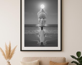 Könnte beinhalten: Ein gerahmter Schwarz-Weiß-Kunstdruck, der eine surreale Szene zeigt: Eine Person steht am Strand und blickt auf einen riesigen, leuchtenden Kopf, der aus dem Ozeanhorizont ragt. Die Person trägt ein langes, helles Gewand unter einem hellen Vollmond.