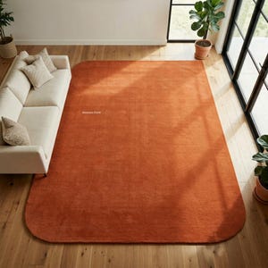 May include: A large, rectangular area rug with rounded corners in a solid burnt orange color. The rug features a smooth, uniform texture and is positioned on a light-colored wooden floor. The text Weavers Point is visible on the rug surface.