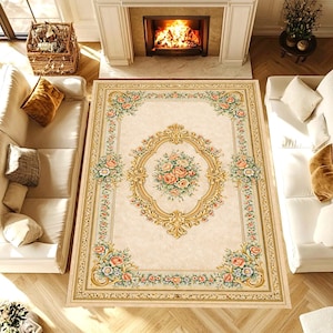 May include: A rectangular area rug with a cream-colored background and a floral design. The rug features a central oval medallion with a bouquet of pink and peach roses, surrounded by a gold frame. The border has floral patterns in pink, green, and gold.