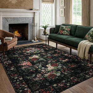 Op de afbeelding: Een groot, rechthoekig vloerkleed met een donkere achtergrond en een bloemenpatroon in rood, roze en wit. Het vloerkleed ligt in een woonkamer met een groene bank en een open haard. Afmetingen: ongeveer 240 x 300 cm.