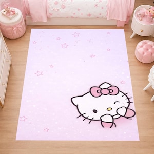 Op de afbeelding: Een rechthoekig roze tapijt met een Hello Kitty-ontwerp. Het tapijt heeft een lichtroze achtergrond met verspreide sterren en een grote illustratie van Hello Kitty met een roze strik en een hart. Het tapijt ligt op een houten vloer.