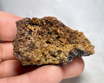 May include: A close-up of a rough, irregularly shaped rock. The rock has a textured surface with a mix of brown, yellow, and dark gray colors. The rock appears to be a mineral specimen.