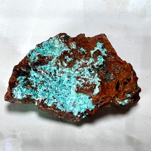 Può includere: Un esemplare minerale grezzo con un mix di trame e colori. La superficie della roccia è principalmente di un marrone rossastro scuro, con chiazze di formazioni cristalline turchese-blu vibranti. Il contrasto crea un effetto visivo sorprendente.