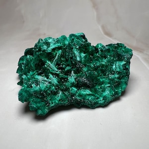 Op de afbeelding: Een levendig, getextureerd malachiet exemplaar. Het mineraal vertoont een rijke, diepgroene kleur met een kristallijne structuur. Het oppervlak heeft een complex, gelaagd uiterlijk, dat de natuurlijke schoonheid van de steen laat zien.