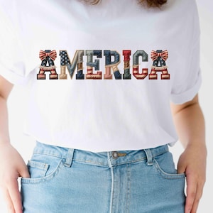 Peut inclure: T-shirt blanc avec le mot "AMERICA" dans un design patriotique. Les lettres sont décorées de motifs du drapeau américain, de nœuds et d'autres éléments patriotiques. Le t-shirt est associé à un jean bleu.