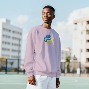K&ouml;nnte beinhalten: Helllila Sweatshirt mit dem Python-Logo in Blau und Gelb. Das Python-Logo befindet sich mittig auf der Brust. Das Sweatshirt ist ein Rundhals-Modell und aus weichem Material.