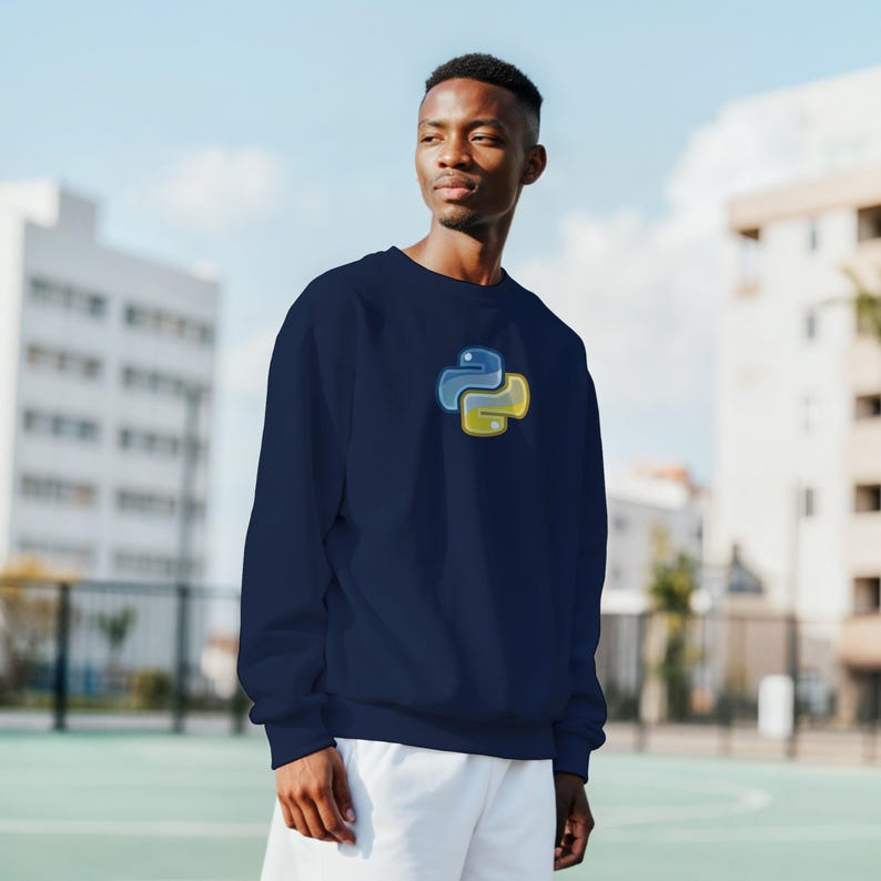 K&ouml;nnte beinhalten: Marineblaues Sweatshirt mit dem Python-Logo in Blau und Gelb auf der Brust. Das Sweatshirt hat einen Rundhalsausschnitt und ist aus einem weichen Material gefertigt. Im Hintergrund sind ein Geb&auml;ude und blauer Himmel zu sehen.