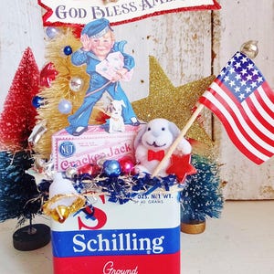 May include: A decorative display featuring a vintage Schilling Ground Allspice tin base, topped with a Cracker Jack box cutout, a sailor boy illustration, a small white plush rabbit, a miniature American flag, and red, white, and blue bottle brush trees.