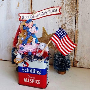 May include: A decorative display featuring a vintage Schilling Ground Allspice tin as a base, topped with a Cracker Jack box, a sailor figure, a small white dog, a gold glitter star, and a miniature American flag with the text God Bless America.