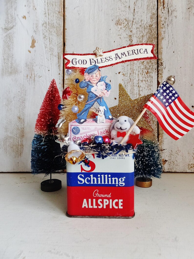 May include: A decorative display featuring a vintage Schilling Ground Allspice tin as a base, topped with a Cracker Jack box, a sailor figure, a small plush rabbit, a miniature American flag, and bottle brush trees in red, white, and blue.