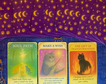 May include: A deck of tarot cards with a purple and gold design featuring moons, stars, and paw prints. Three cards are face up, displaying illustrations of cats and text: "SOUL PATH", "MAKE A WISH", and "THE GIFT OF TRANSFORMATION".